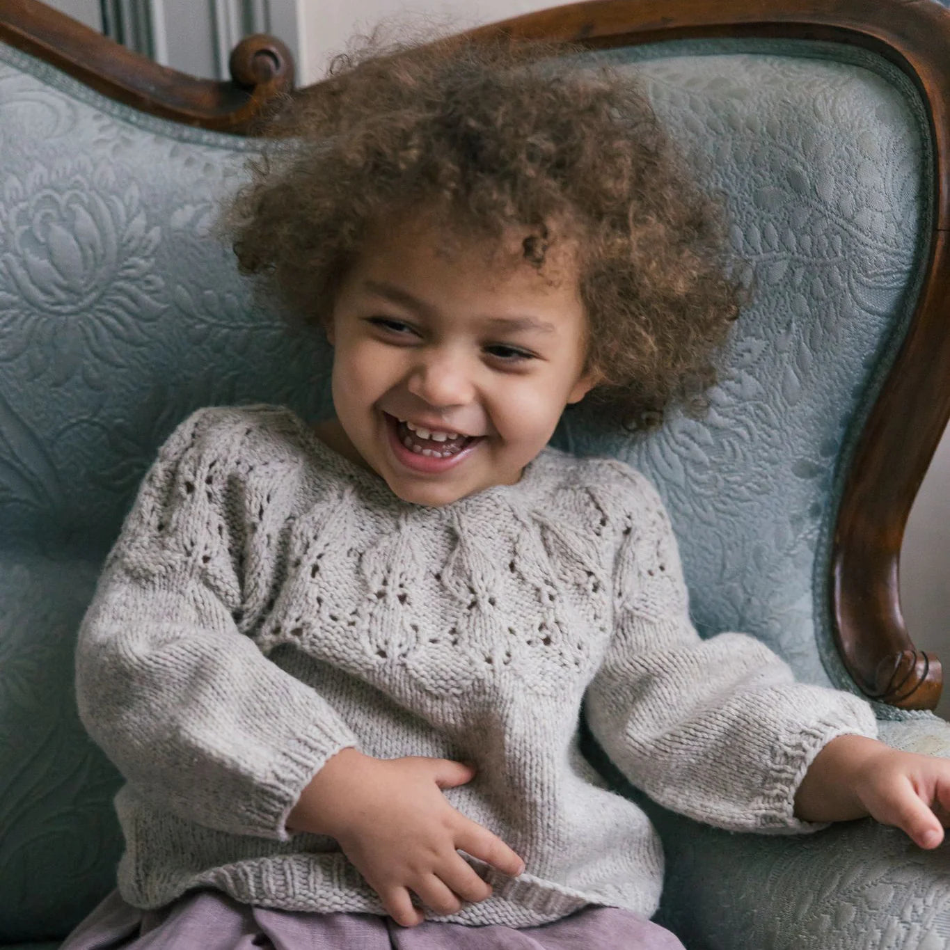 Child laughing while wearing an intricately knit gray sweater