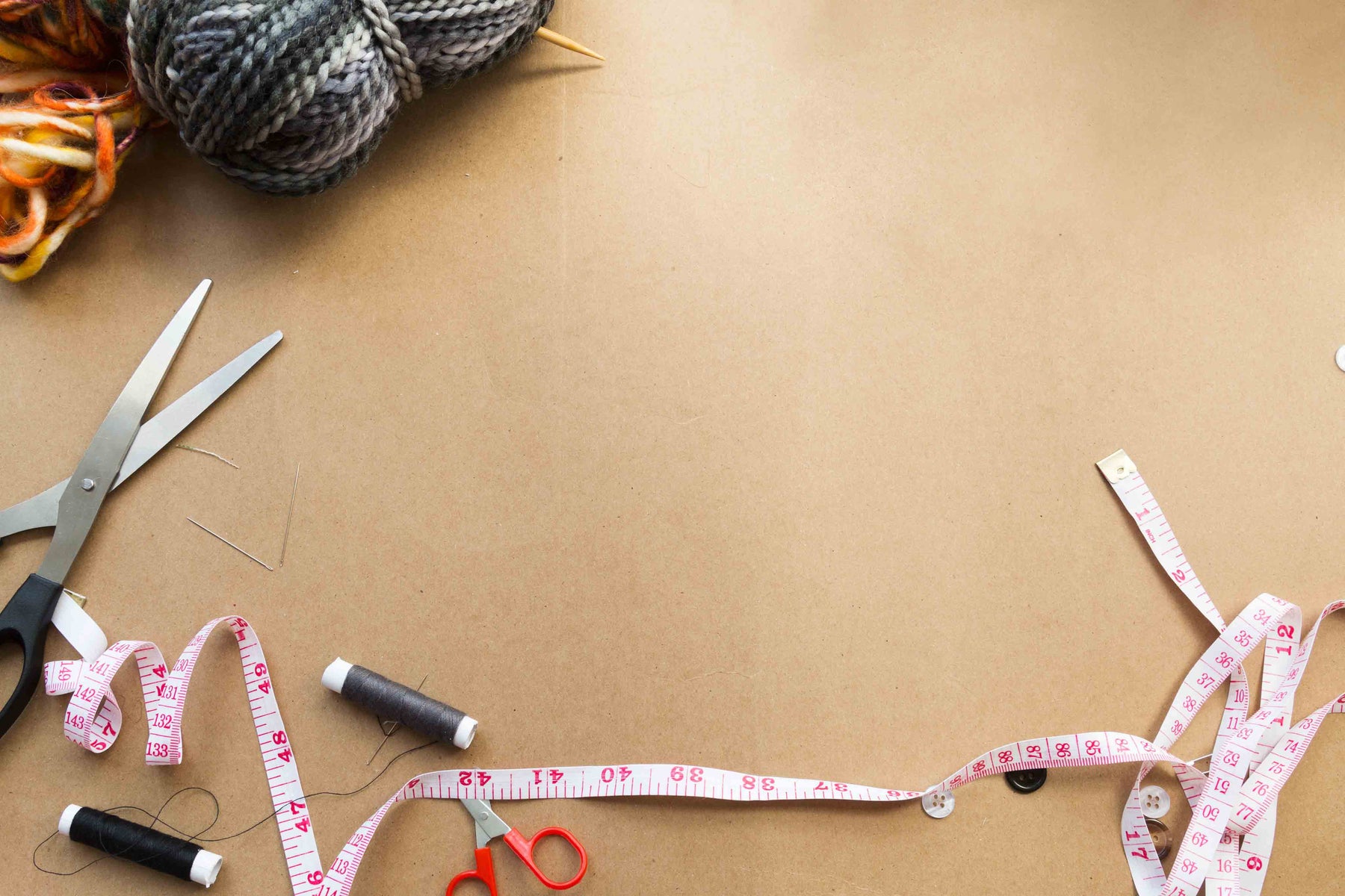 sewing supplies, yarn, and a measuring tape on a parchment paper background