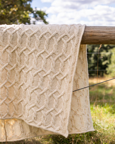 Cream cable knit blanket draped over a fence