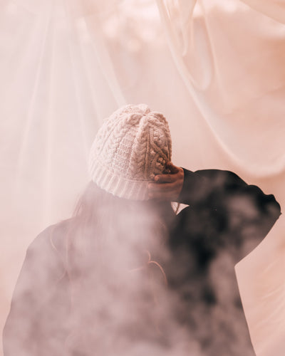 woman wearing a white knit hat with pink fog around her